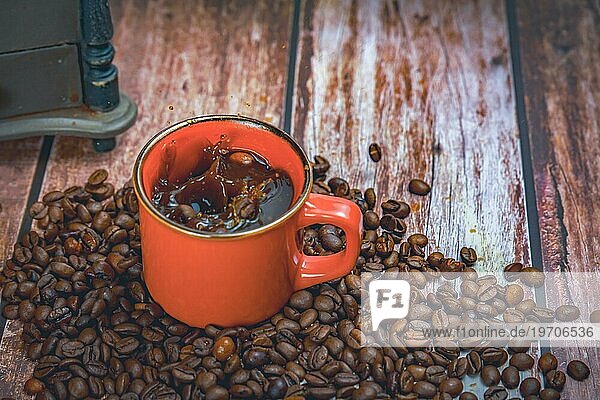 Rote Kaffeetasse mit Kaffeebohnen fallen im Inneren mit Splash Effekt splash im Hintergrund eine manuelle Kaffeemühle