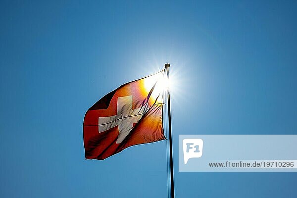 Schöne Schweizer Flagge gegen blauen klaren Himmel und Sonnenstrahl in einem windigen Tag in der Schweiz