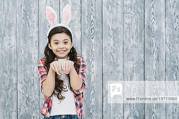 Lächelndes Mädchen mit Hasenohren  das wie ein Kaninchen vor einem grauen Holztisch posiert
