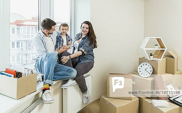 Glückliche Familie sitzt auf der Fensterbank mit Umzugskartons in ihrem neuen Zuhause