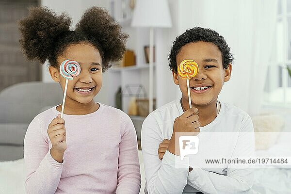 Vorderansicht zwei lächelnde Geschwister  die mit Lollipops posieren