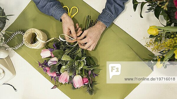 Erhöhte Ansicht männlichen Touristen binden Blumenstrauß mit String grünes Papier Schreibtisch