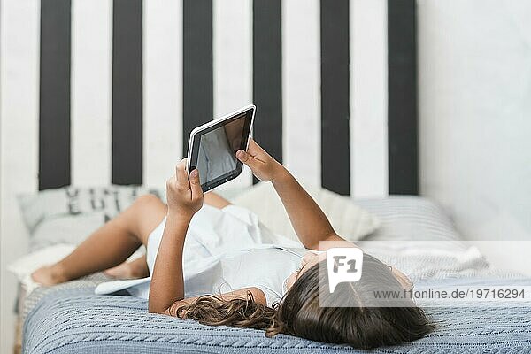 Mädchen im Bett liegend mit digitalem Tablet