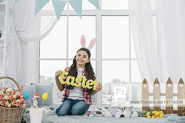 Porträt lächelnd Mädchen sitzt vor Fenster zeigt gelbe Ostern Wort