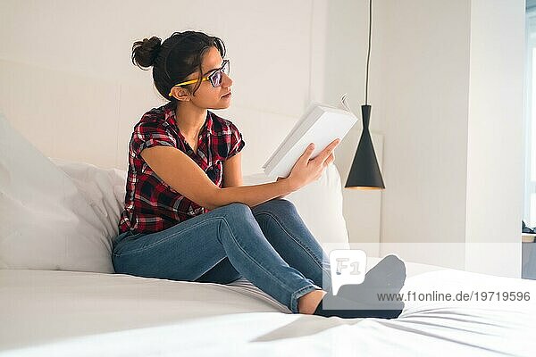 Seitenansicht einer jungen Frau  die bequem in einem Hotel sitzt und ein Buch liest