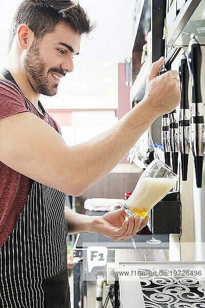 Ein lächelnder junger Barkeeper schenkt frisches helles Bier vom Fass ein