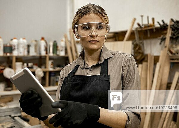 Vorderansicht weiblicher Tischler mit Schutzbrille  der ein Tablet hält