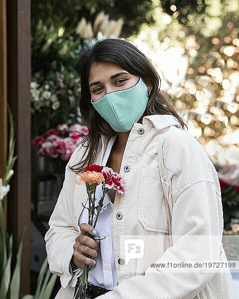 Frau mit Gesichtsmaske posiert im Freien mit Blumen