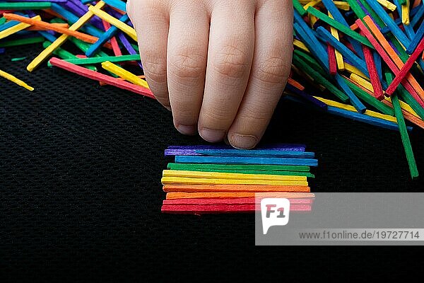 Kind spielt mit farbigen Holzstäbchen für Kreativität auf weißem Hintergrund