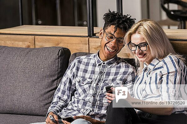 Porträt lächelnd junges Paar sitzt Sofa suchen Handy