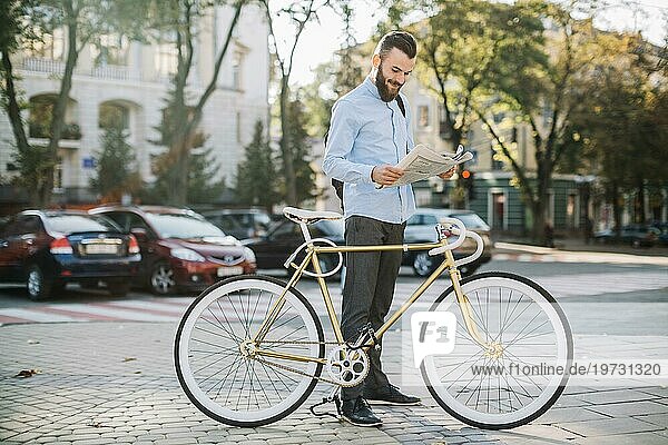 Fröhlicher Mann liest Zeitung in der Nähe des Fahrrads