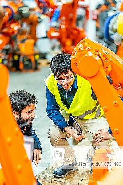 Vertikales Foto von zwei multiethnischen jungen Ingenieuren  die den Betrieb von Roboterarmen in der Fabrik überprüfen