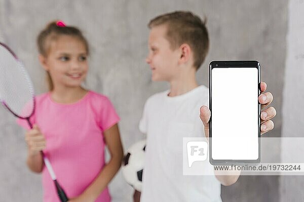 Junge stehend mit Mädchen  das ein Mobiltelefon mit weißem Bildschirm zeigt
