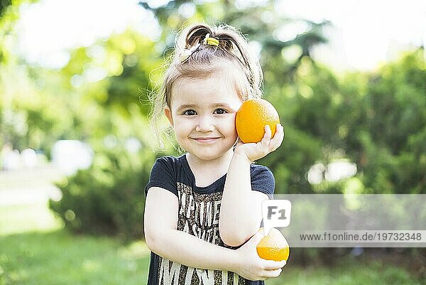 Lächelndes Mädchen hält zwei frische Orangen im Park