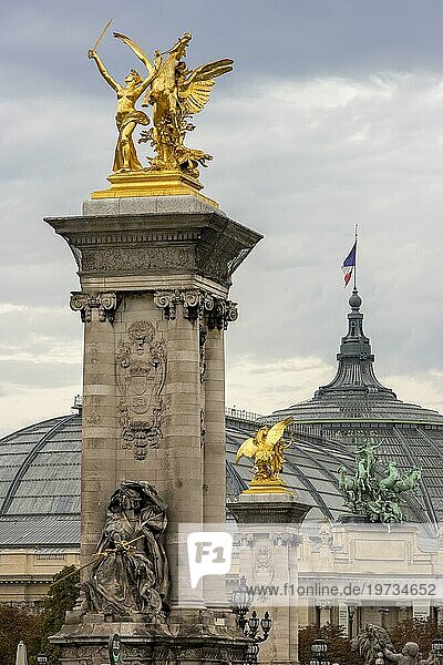 Säulen mit Skulpturen auf der Pont Alexandre III  Neobarocks erschittete Brücke und im Hintergrund eine riesige Skulptur mit Pferden auf dem Grand Palais-Gebäude  Paris  Île-de-France  Frankreich  Europa