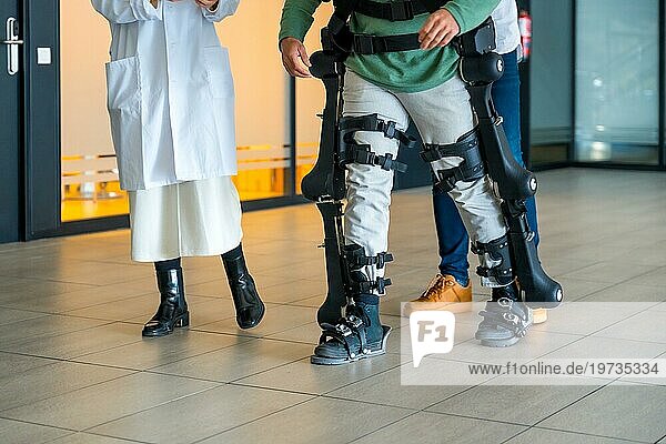 Mechanisches Exoskelett  Ärztin mit nicht erkennbarem Ingenieur geht mit behinderter Person mit Roboterskelett in Rehabilitation  Physiotherapie in einem modernen Krankenhaus  futuristische Physiotherapie
