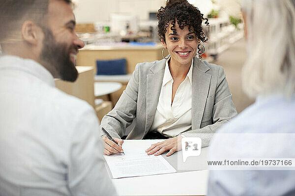 Bank worker signing contract while talking with clients