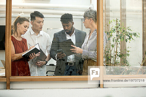 Coworkers discussing project while standing in meeting room