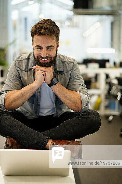 Male entrepreneurhaving a video call on laptop while sitting on table
