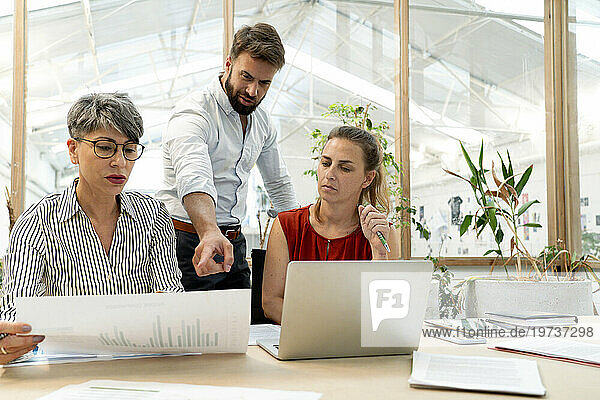 Businessman discussing with colleagues while checking on laptop and paperwork