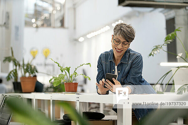Female entrepreneur scrolling on smart phone while leaning on table