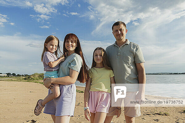 Smiling parents with daughters standing on sand at beach