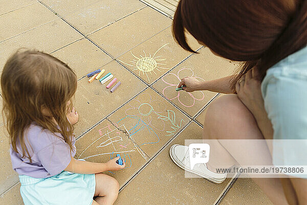 Mother and daughter drawing on tiled floor at park
