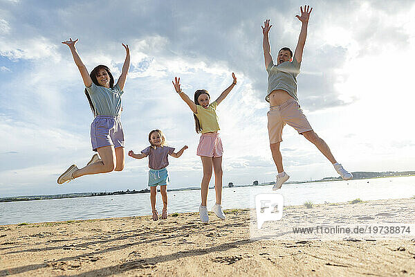 Cheerful parents with daughters jumping at beach