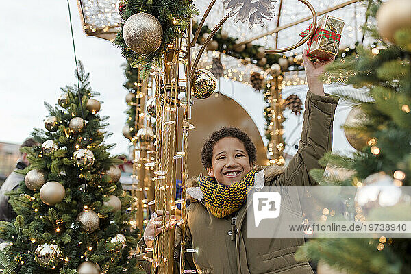Happy boy holding gift box and enjoying near Christmas decoration at market