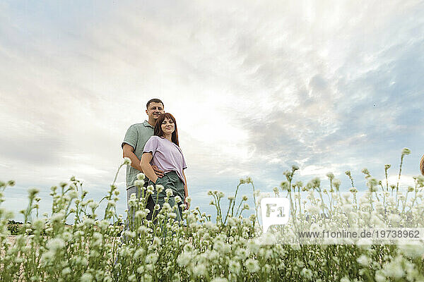 Happy couple standing in flower field under sky