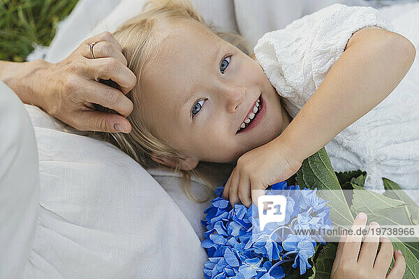 Happy girl with blue flowers lying on mother's lap