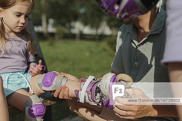 Father helping daughter in putting roller skates at park