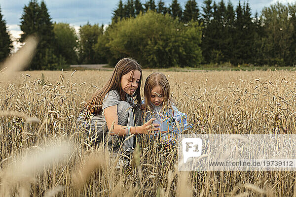 Sisters using smart phone amidst field