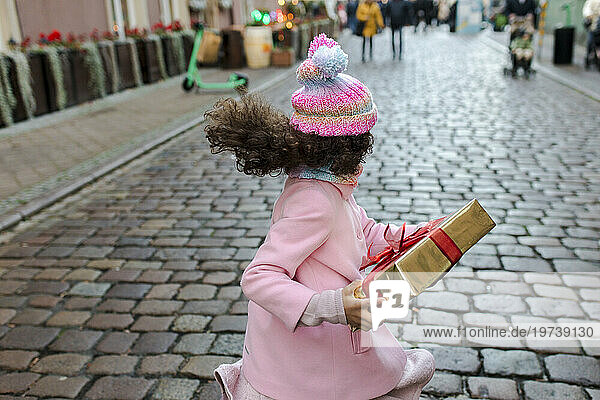 Happy girl holding gift box and running on street