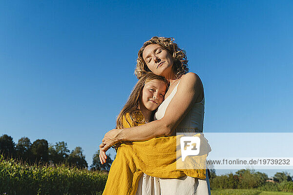 Smiling mother and daughter hugging each other under blue sky
