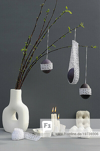 Studio shot of candles burning under laced Easter eggs hanging from twigs in vase