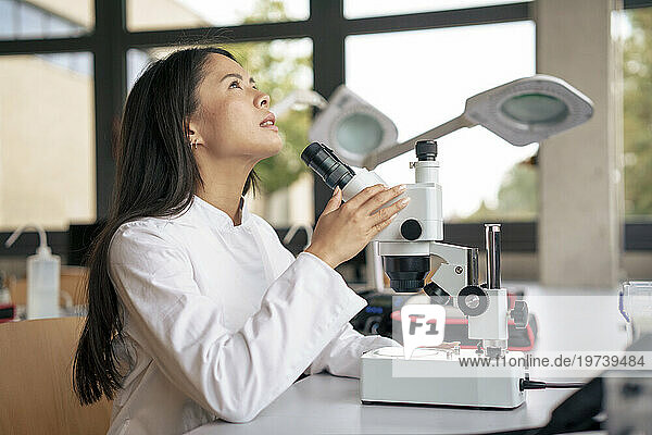 Thoughtful scientist sitting with microscope at desk