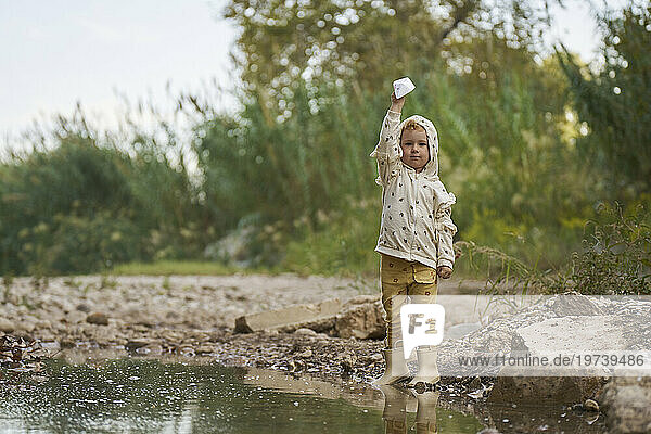 Girl holding paper boat and standing near water puddle