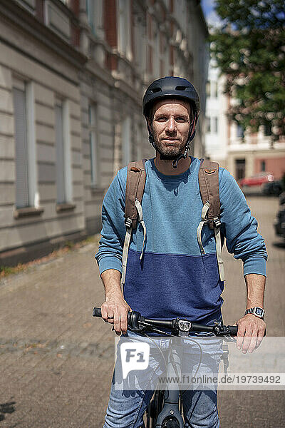 Smiling man wearing helmet standing with bicycle on sunny day
