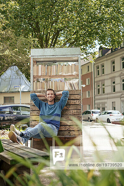 Smiling man sitting and leaning on cabinet of books