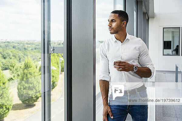 Casual businessman looking out of window holding cup of coffee