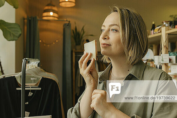 Thoughtful blond woman smelling soap bar in retail store