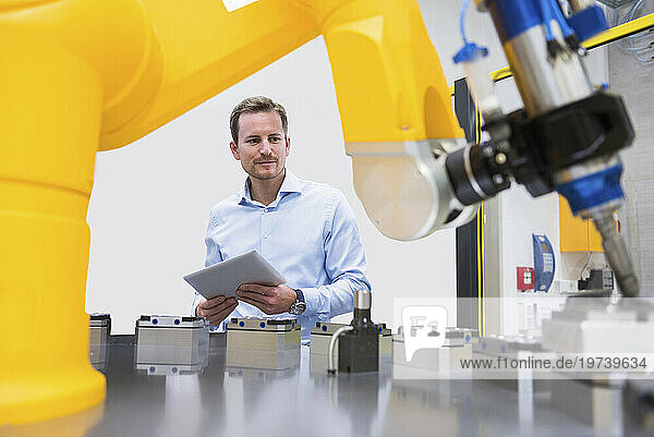 Engineer holding tablet PC and examining robotic arm in factory
