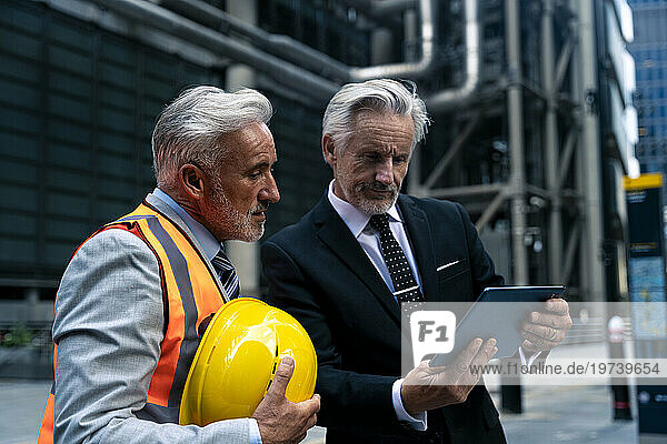 Senior businessman discussing and using tablet PC near building