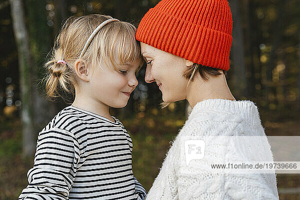 Smiling mother wearing knit hat and embracing daughter in forest