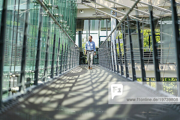Businessman walking in corridor of modern office building carrying digital tablet