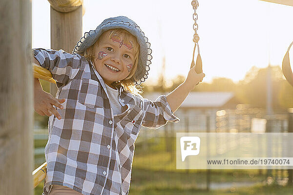 Smiling girl with face paint playing in playground at sunset