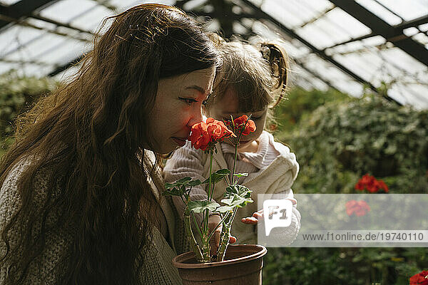 Mother carrying daughter and smelling red flowers in greenhouse