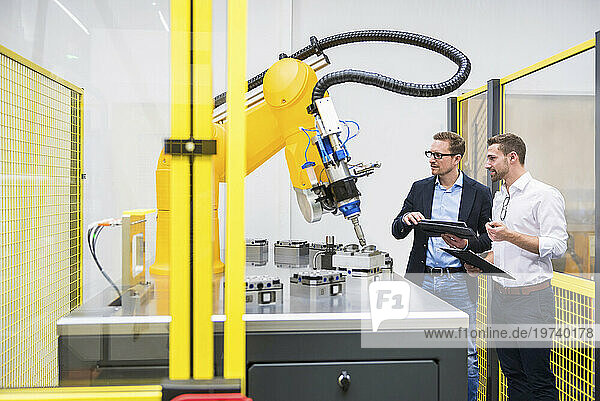 Engineers with tablet PC examining robotic arm in factory