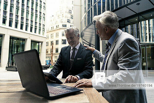 Smiling businessman discussing with colleague over tablet PC at table